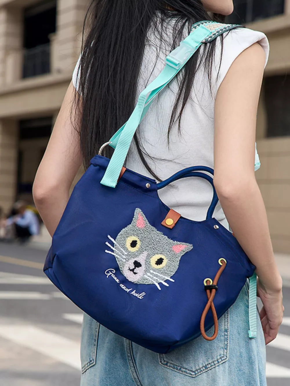 Actual dark blue cat handbag worn over the shoulder with its adjustable aqua patterned strap