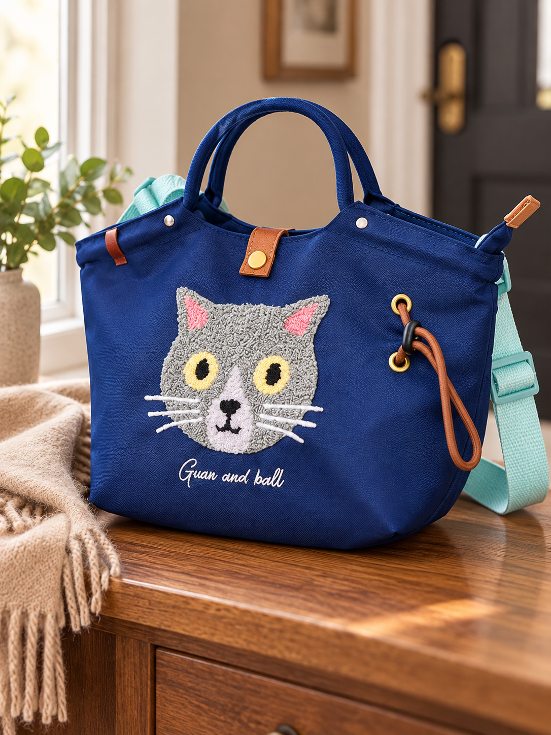 Close view of cat embroidery, top handle and cord accent on the dark blue Oxford-cloth bag