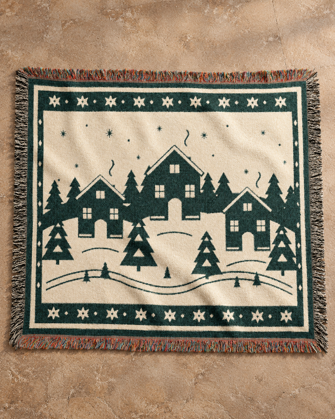 Cream and forest-green Family Winter Story woven cotton blanket, complete fringes shown on warm tan stone.