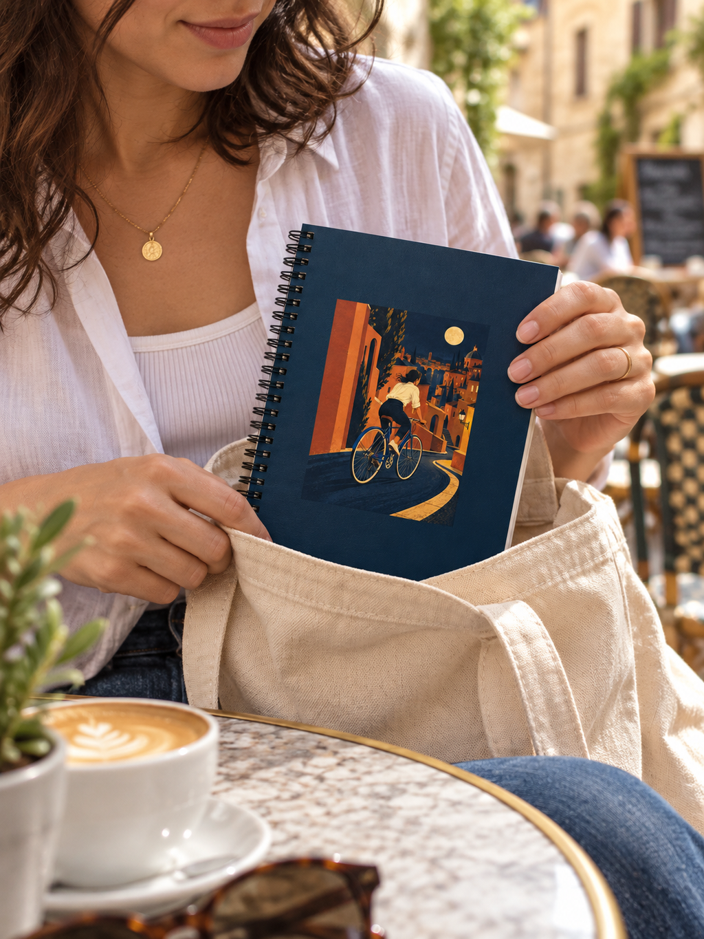 A person taking the Night Ride spiral notebook from a canvas bag at a city cafe