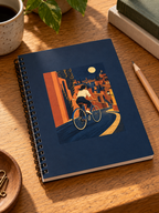 Night Ride notebook print, black metal spiral binding and paper cover detail on an oak desk