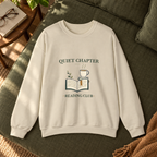 Quiet Chapter Reading Club Sand crewneck on an olive linen daybed; lifestyle mockup.